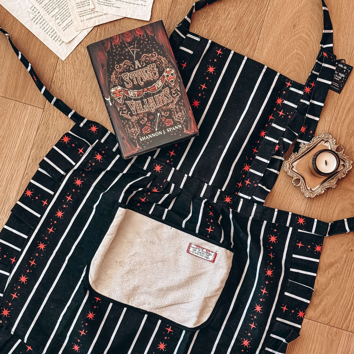The Night Circus-inspired apron lies on a wooden floor next to a book and a candle.