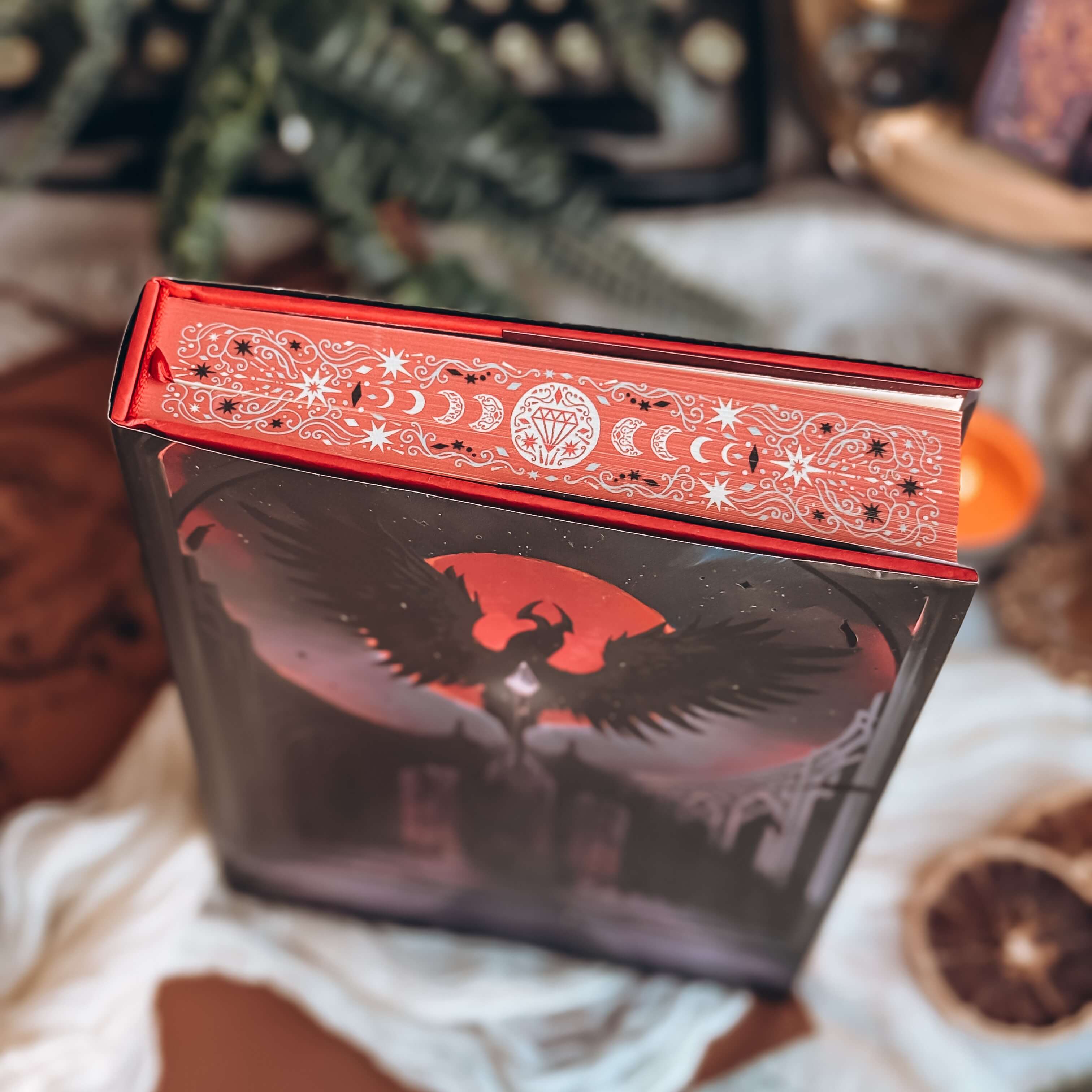 Stenciled edges of The Dark is Descending by Chloe C Peñaranda showing various fantasy elements and the phases of the moon on a red background.