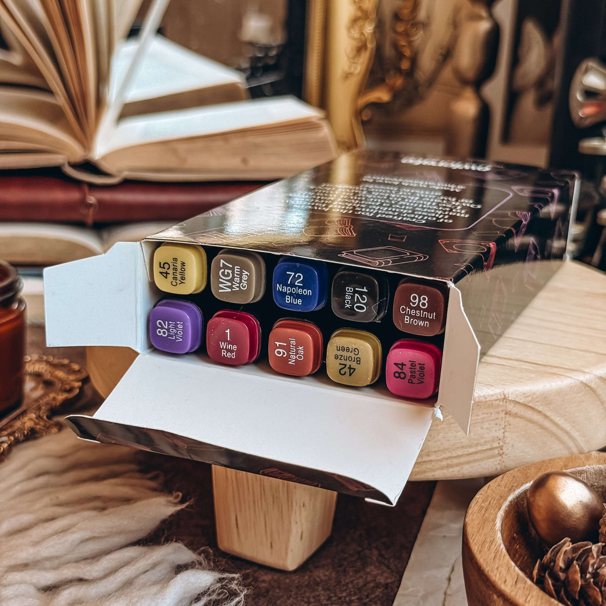 An open carton of Fantasy Artist Markers rests on a wooden stand. All ten markers in various colours are shown in the open box.