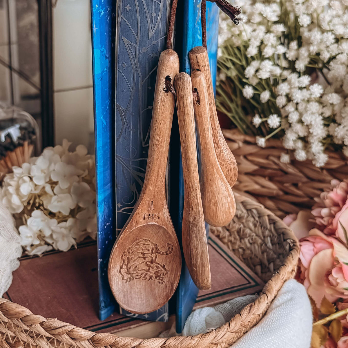 Six Crimson Cranes-inspired wooden measuring spoons held up by a book with blue sprayed edges.