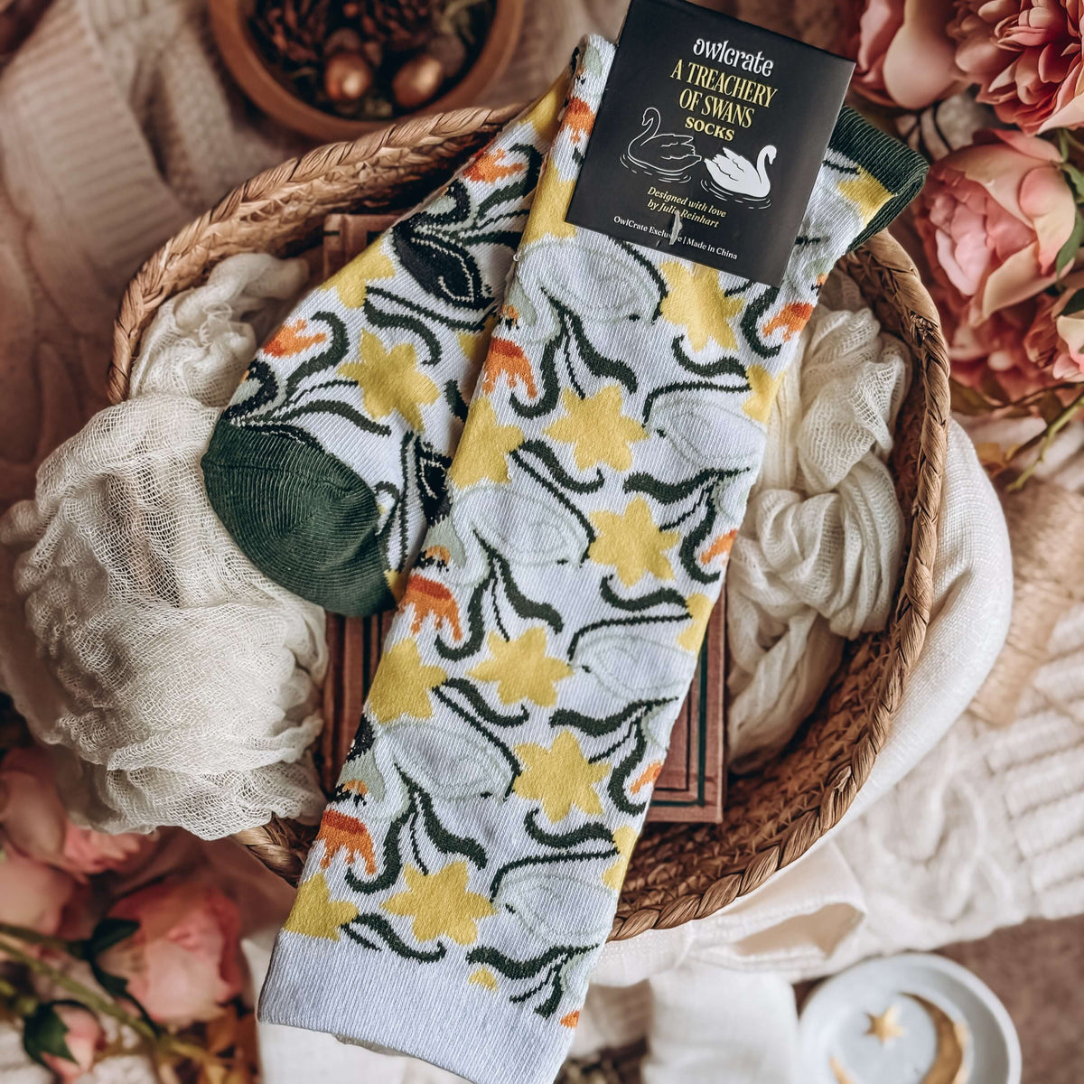 A Treachery of Swans-inspired socks with soft cloths, linens, and flowers in the background.