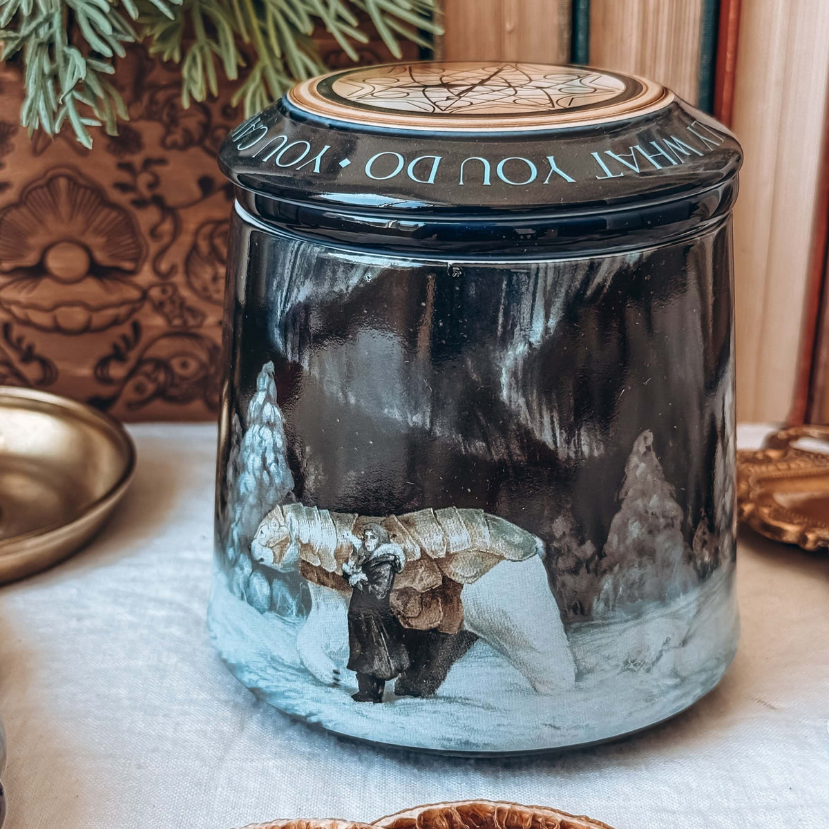 A close-up of a ceramic mug and lid, featuring artwork showing an armoured bear next to a small girl in a snowy landscape.