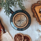 A top-view of a ceramic mug lid featuring the quote 'You cannot change what you are, only what you do' circling a depicting of a gold-coloured fantasy compass. The mug is surrounded by various holiday-themed decorative items.  