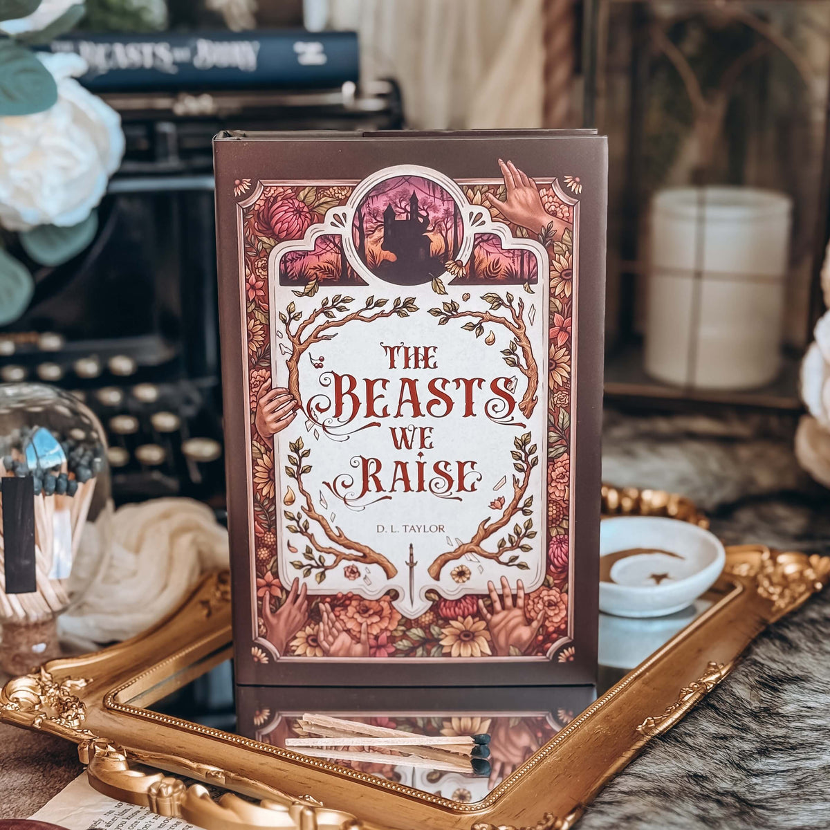 The front cover for the book titled The Beasts We Raise by D.L. Taylor featured on a gold mirror, surrounded by various decorative items.