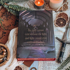Back cover of The Dark is Descending by Chloe C Peñaranda with the text "The dark cannot exist without the light and light cannot exist without the dark." Cover shows an illustrated dark fantasy throne room. Book is surrounded by decorative items, such as a candle, a knife, and a map. 
