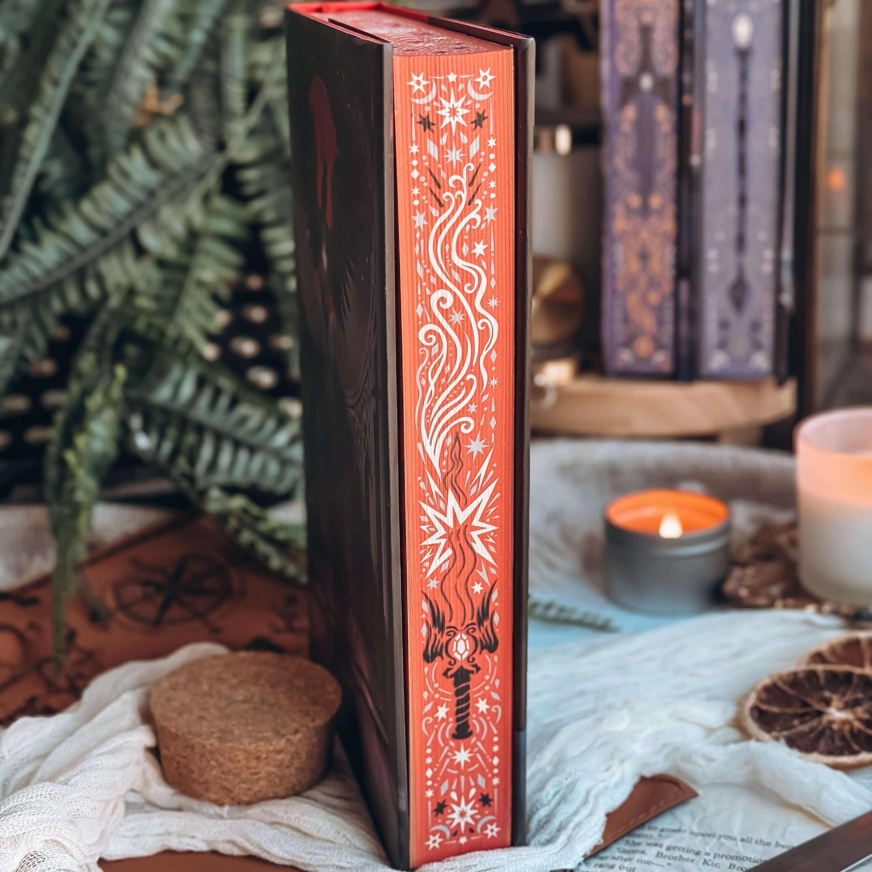 Stenciled edges of The Dark is Descending by Chloe C Peñaranda showing a sword with intricate fantasy details on a red background. 