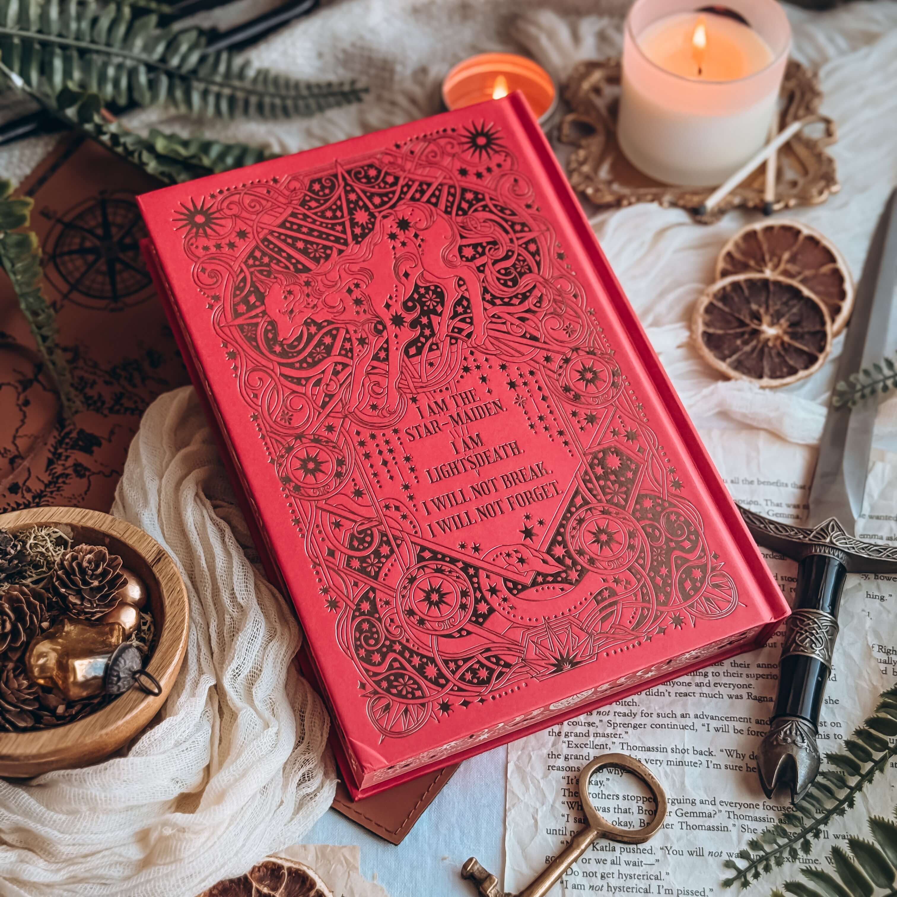 Hardcover book of The Dark is Descending by Chloe C Peñaranda showing a red book with ornate black embossing. Text reads "I am the star-maiden. I am light's death. I will not break. I will not forget."