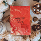 The back cover for the book Dreamland by Olivie Blake showing a red and orange marbling effect that merges into flames and illustated roses with the quote 'Every story ends in death' centered. The book is styled on a wooden pedestal surrounded by decorative items.
