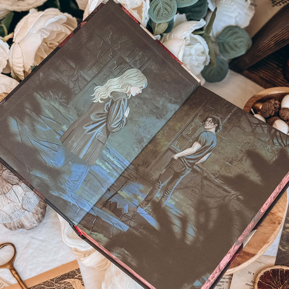The front illustrated endpapers for the book Dreamland by Olivie Blake showing a man and woman standing in a derelict room. The open book is styled among white fabric, white flowers, and other decorative items. 