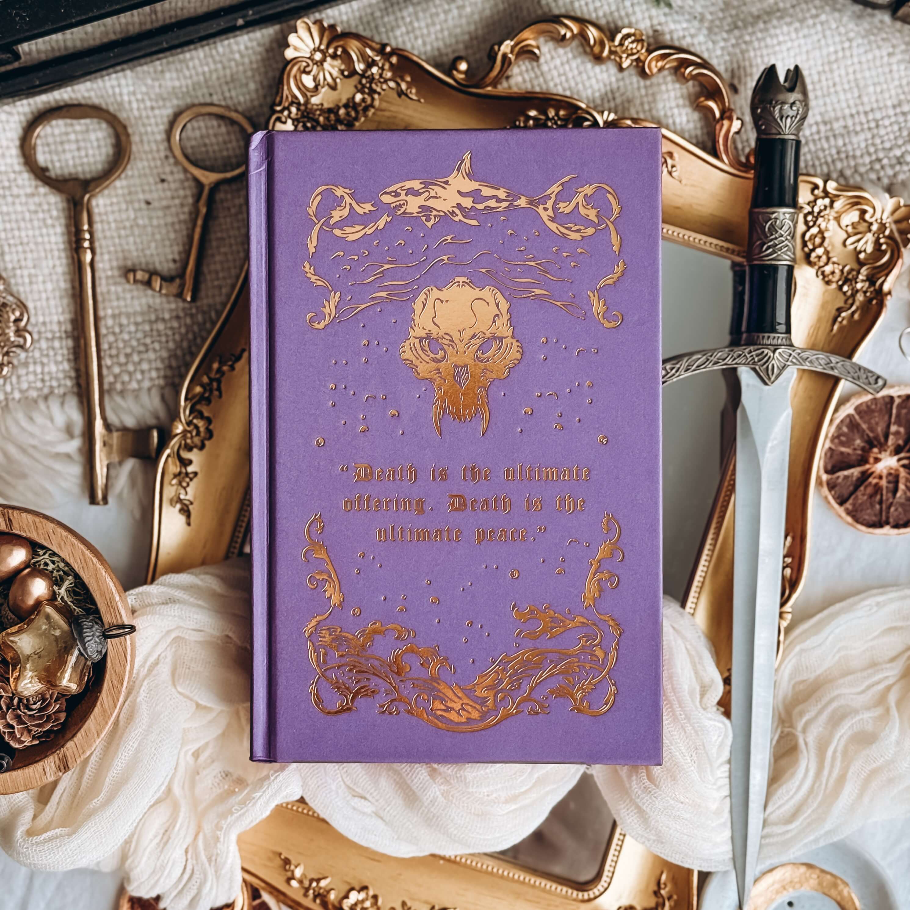 Hardcover of The Fallen and the Kiss of Dusk by Carissa Broadbent. The purple book features gold embossing fantasy details and the text reading "Death is the ultimate offering. Death is the ultimage peace."