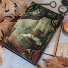 A hardcover book featuring an illustrated scene of a bed in an old, ancient, forest bog. The book is centered among various leaves, open books, an antique key, and a pocket watch. 