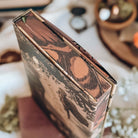 A close-up of the detailed stencilled edges of a hardcover book surrounded by various vintage-inspired decor in the background. The stencilled edges resemble a vintage close-up illustration of a butterfliy's wing in shades of orange.