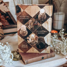 The back of a hardcover book stands updright on an old book, surrounded by baby's breath flowers and other rustic decor. The back cover is styled after a vintage brown and cream wooden chess board with small illustrated scenes and chess pieces.