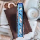 Stenciled edges for Starter Villain by John Scalzi, showing illustrated depictions of cats in various positions, separated by cat paw prints on a blue background. 