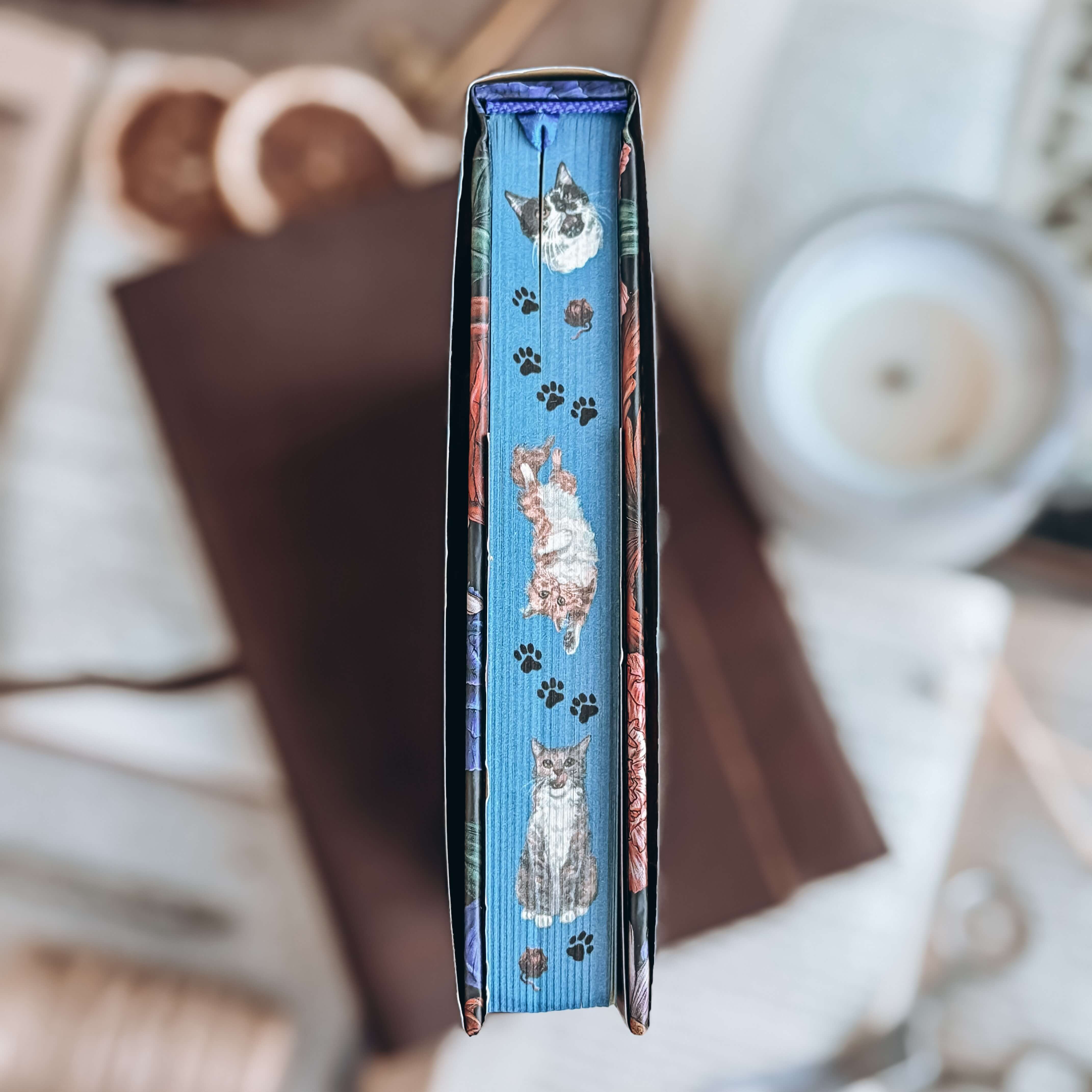 Stenciled edges for Starter Villain by John Scalzi, showing illustrated depictions of cats in various positions, separated by cat paw prints on a blue background. 