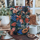 Hardcover of Starter Villain by John Scalzi. Decorated floral book includes text reading "See you in Hell. Not Soon enough." Book is surrounded by decorative items. 