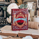 The front of a book-shaped vase modeled after a copy of Les Miserables sits on an open book with twine, white flowers, and a typewriter in the background.