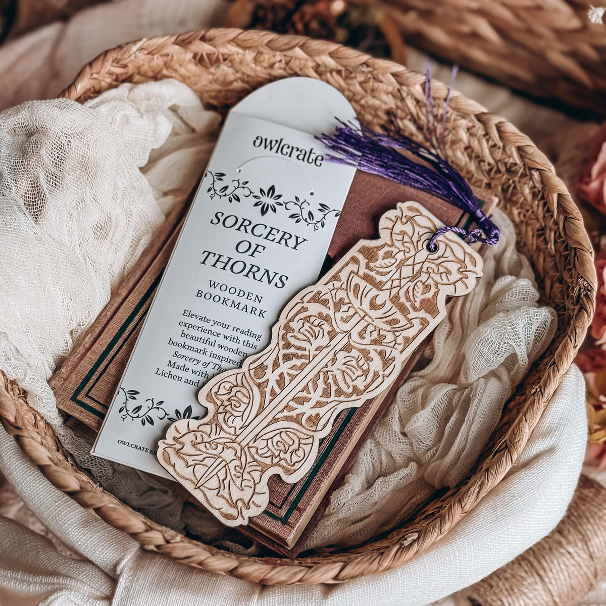 Sorcery of Thorns-inspired wooden bookmark lies on top of a paper envelope and a brown book, all resting in a wicker basket.