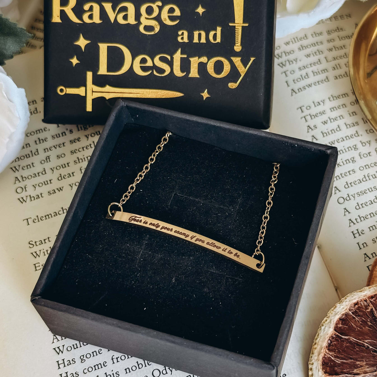 A gold bracelet in a black velvet box sits next to the top of the box, both on top of an open book.