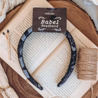 A black fabric headband with a pattern made of pages and decorative designs rests on an open book, surrounded by a roll of twine and matchsticks.