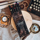 A carton of Fantasy Artist Markers rest on a wooden stand, with five markers poking out the open top. Marker carton is surrounded by candles, papers, and a typewriter.