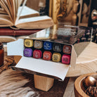 An open carton of Fantasy Artist Markers rests on a wooden stand. All ten markers in various colours are shown in the open box.