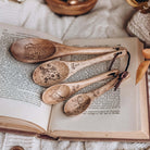 Six Crimson Cranes-inspired wooden measuring spoons resting on an open book.
