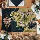 A tea towel depicting the map of Middle-earth is centered, surrounded by white flowers, open books, a tassle scarf, and a bowl of potpouri.