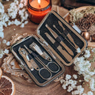 An open toiletry set, featuring a variety of silver instruments, is centered with baby's breath flowers, a bowl of potpouri, and a lit candle in the background.