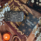 A black case and a black cardboard box of the toiletry set lies on a book with baby's breath flowers, a lit candle, and a typewriter surrounding.