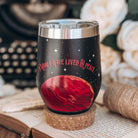A black tumbler sits on a cork stand, with a roll of twine, a typewriter, and white flowers in the background.